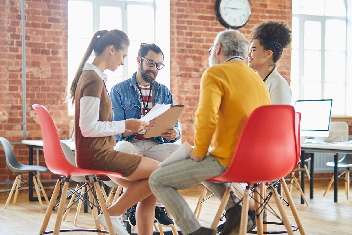 Group of four colleagues sitting on chairs and discussing data or their new ideas for new business project